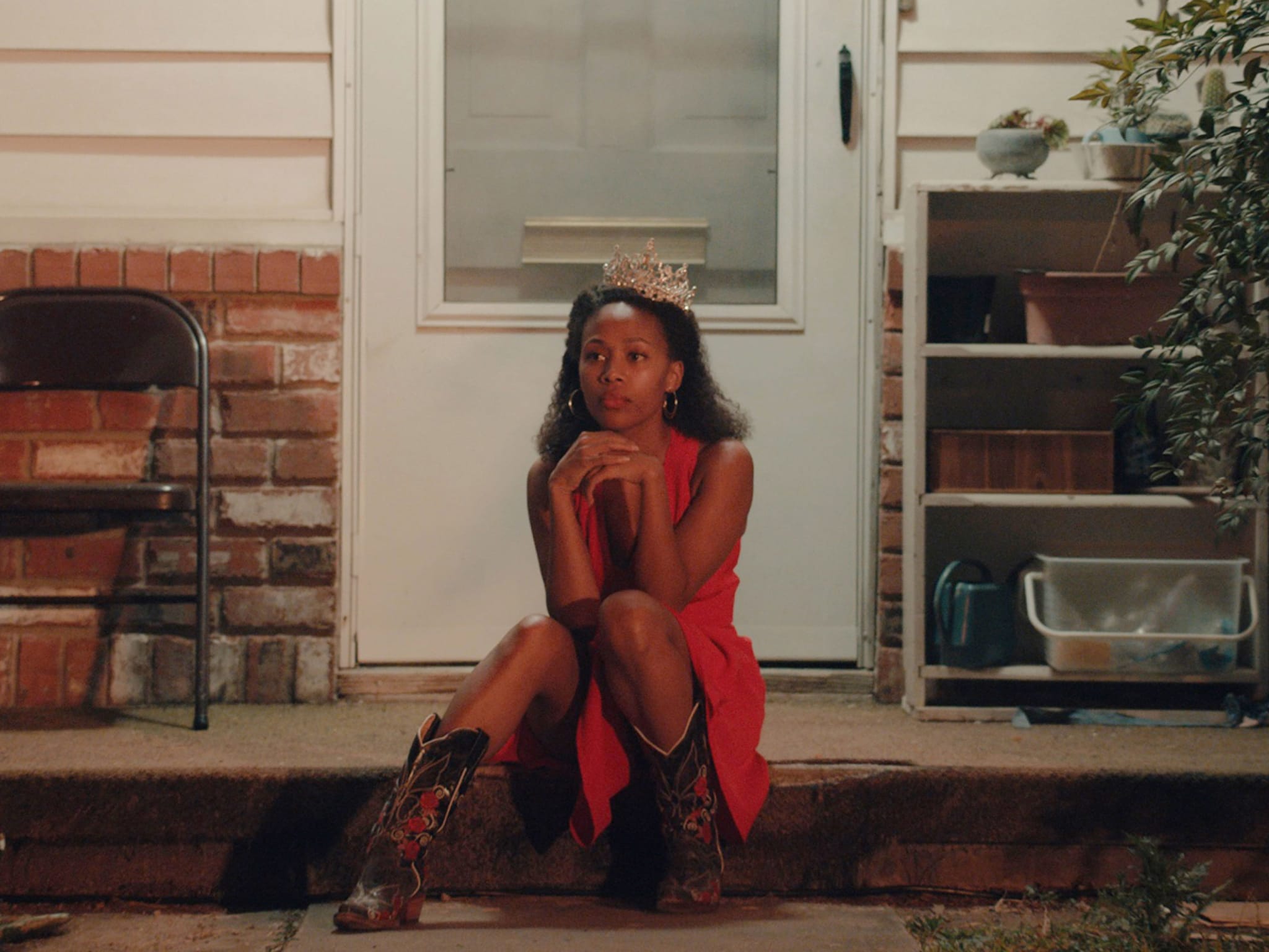 A woman wearing a crown sitting on the porch of a house.
