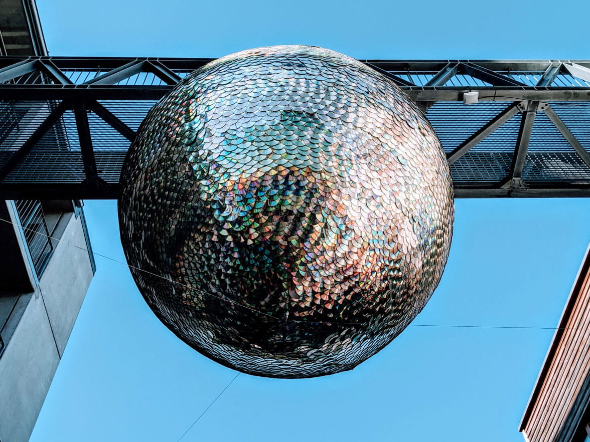 A large mirrorball hanging on a structure outside.