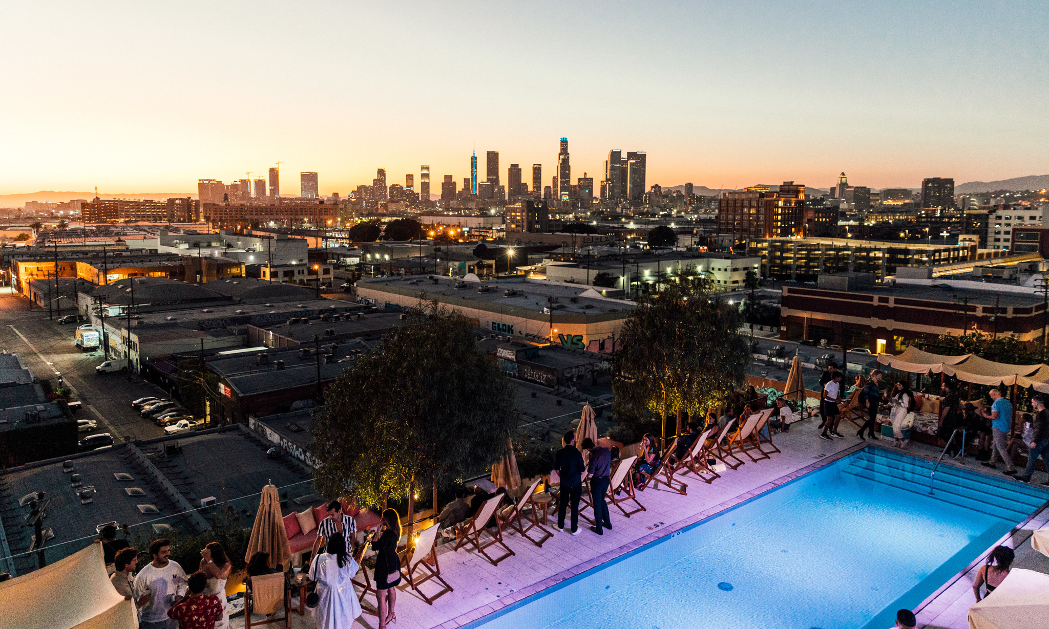 People standing around a rooftop pool at sunset with a city in the background.