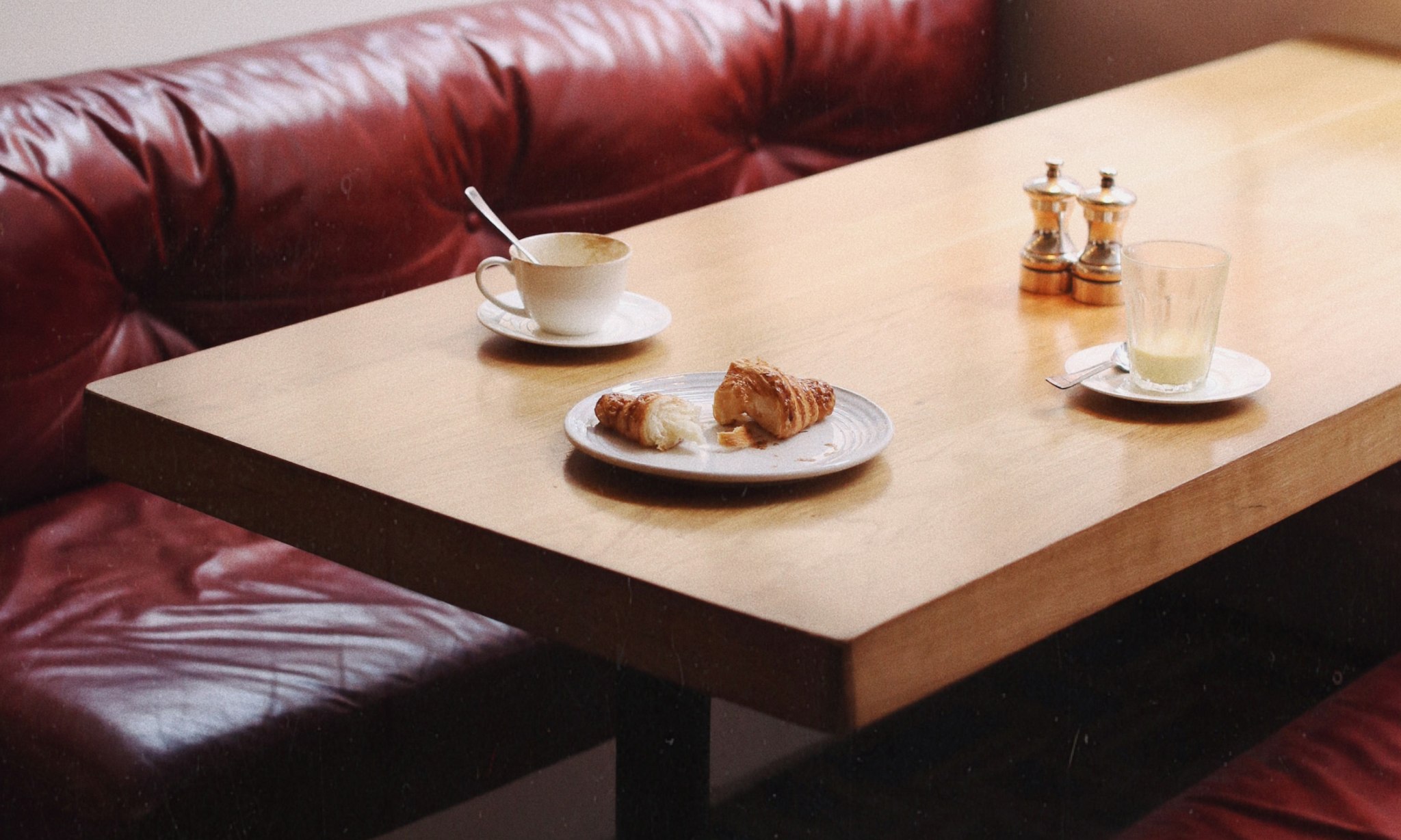 A table with a half eaten croissant on it and two drinks.