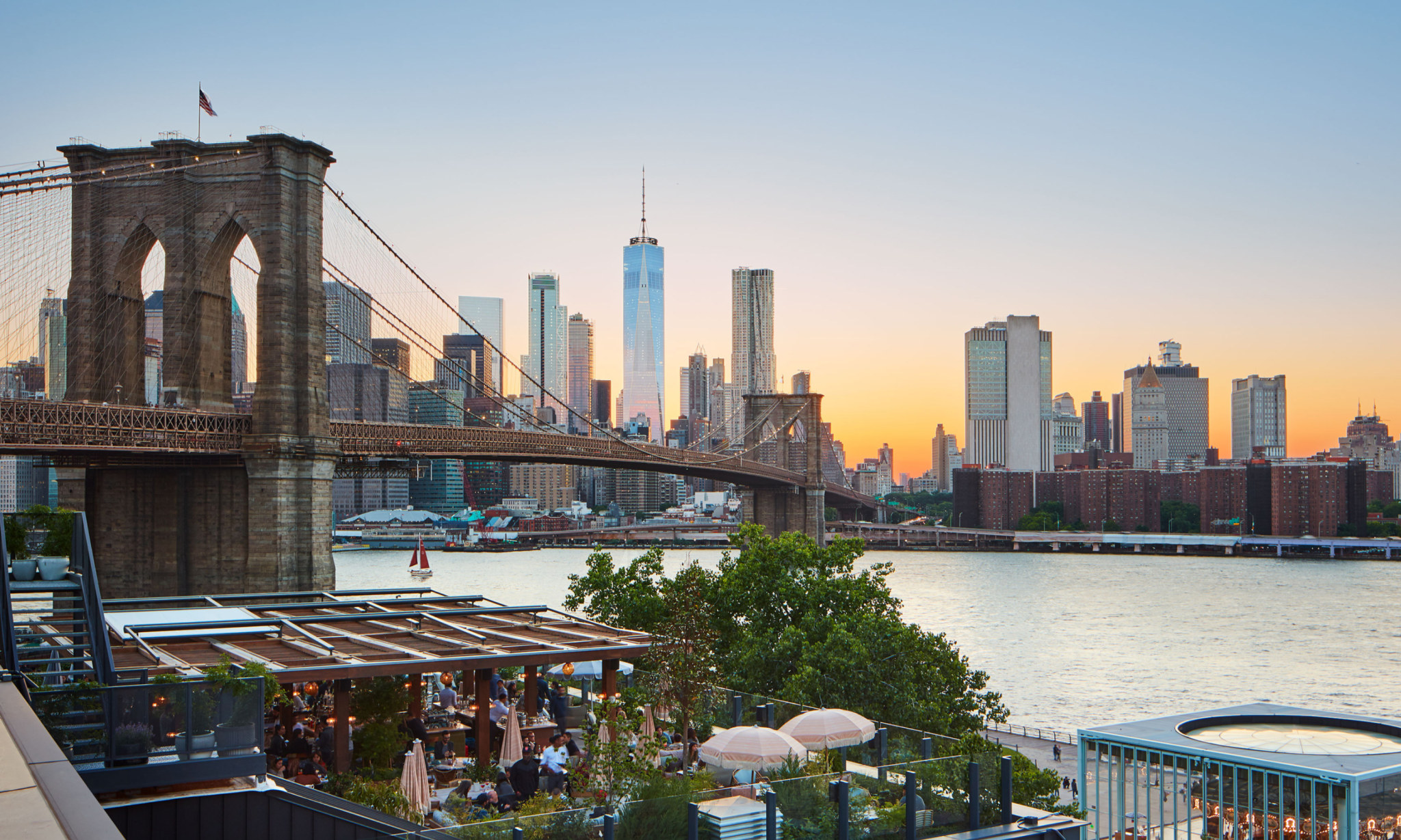 A restaurant's terrace overlooks the East River, Brooklyn Bridge and downtown Manhattan at sunset.
