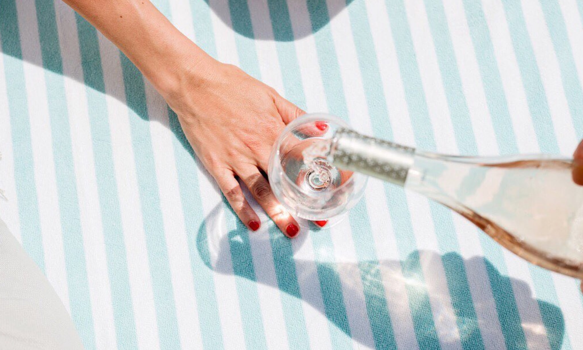 A hand steadies a glass with wine being poured into it.