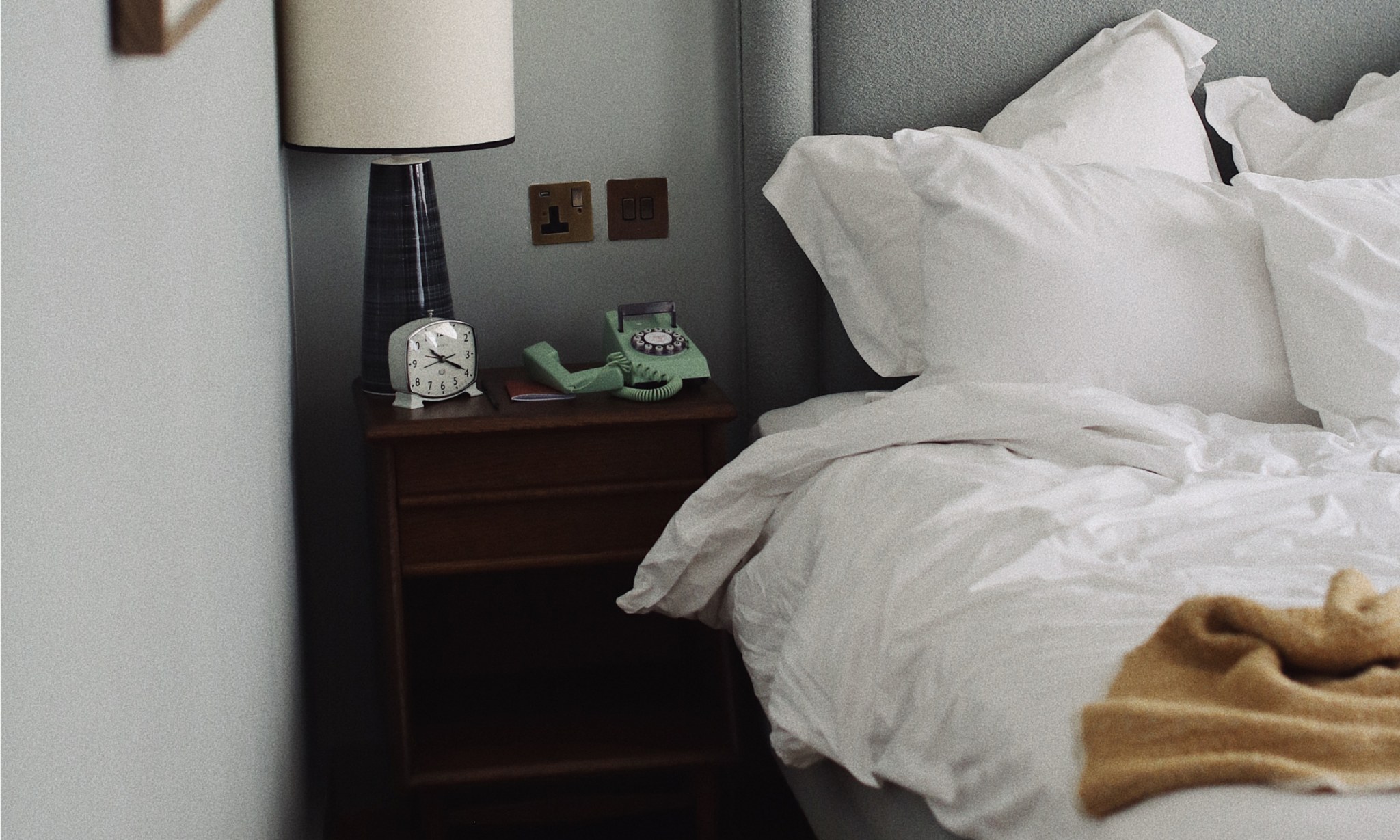 An unmade bed next to a phone off its hook.