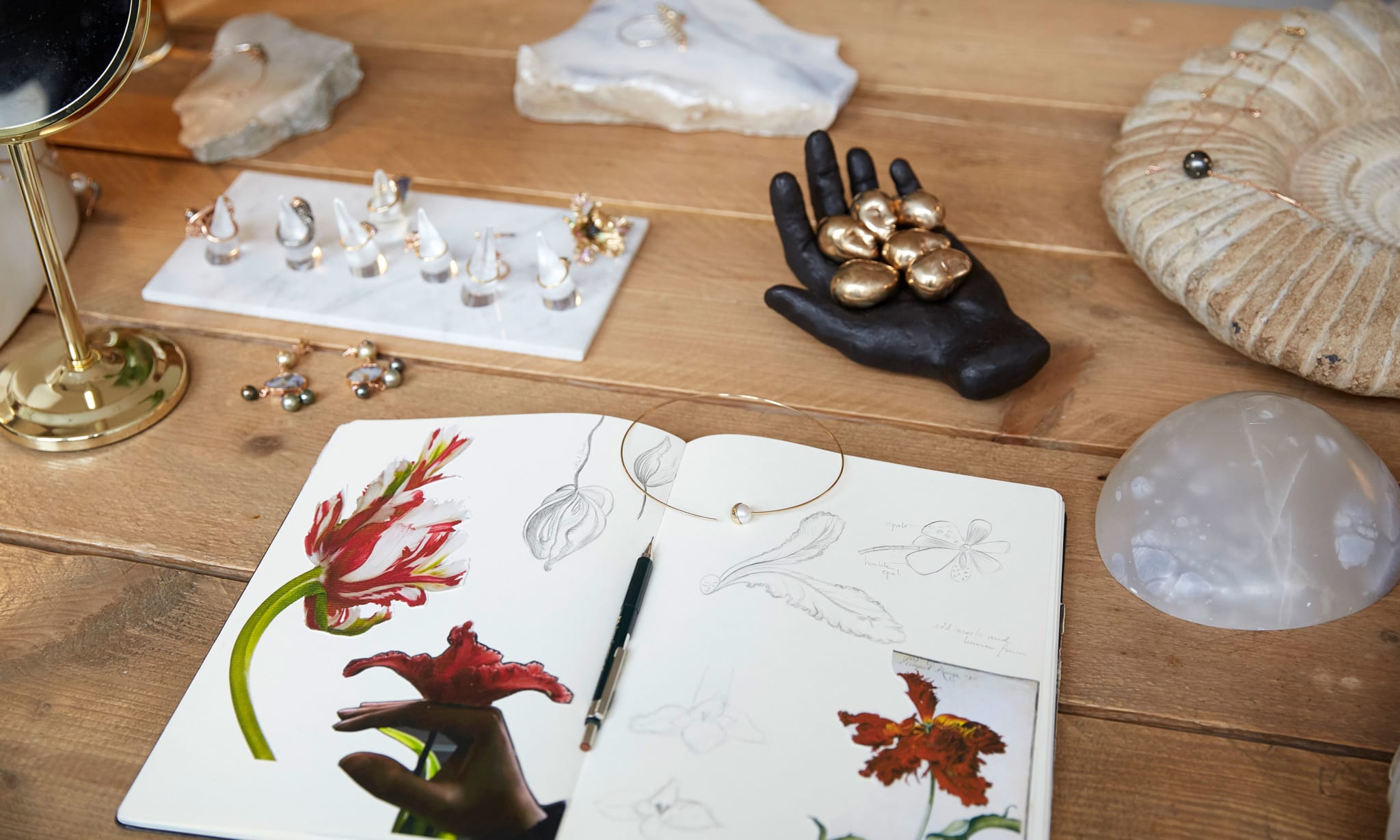 A wooden table with a sketch book and jewellery on it.