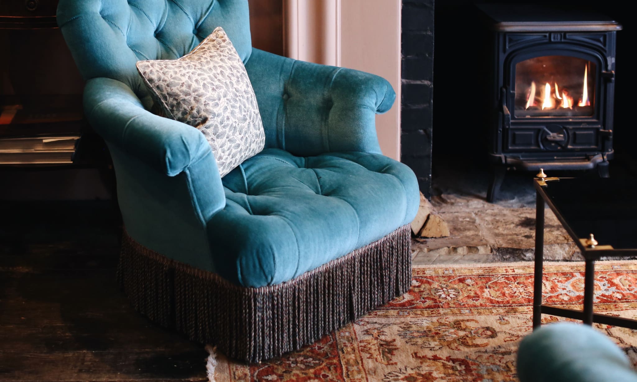 A blue armchair on a rug next to a lit wood burning stove