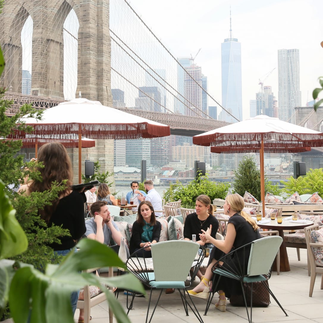 Outdoor seating and dining area surrounded by plants and next to an outdoor bar.