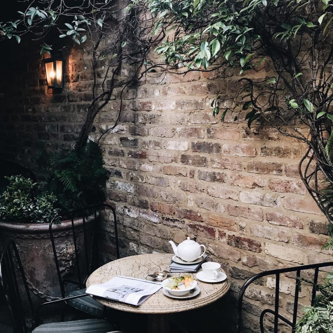 A outdoor terrace area with brick walls, plants and a table and chairs with a tea set laid on it.