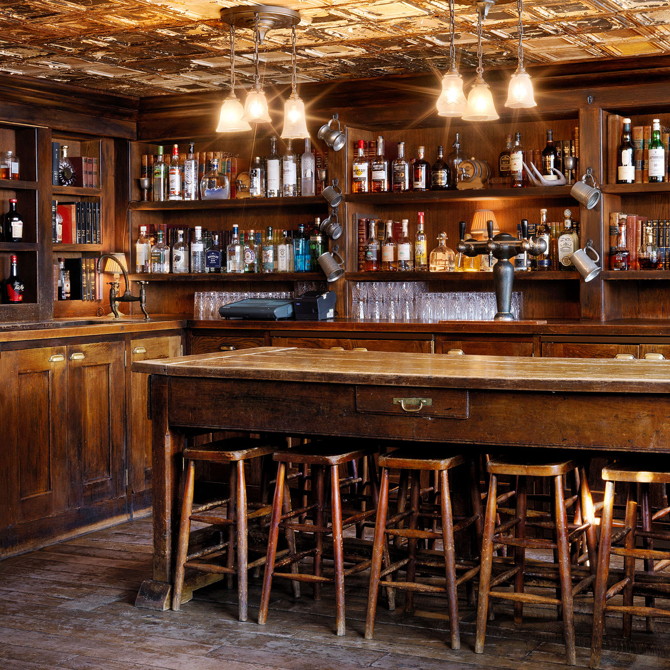 A wood panelled bar with a long table and stools.
