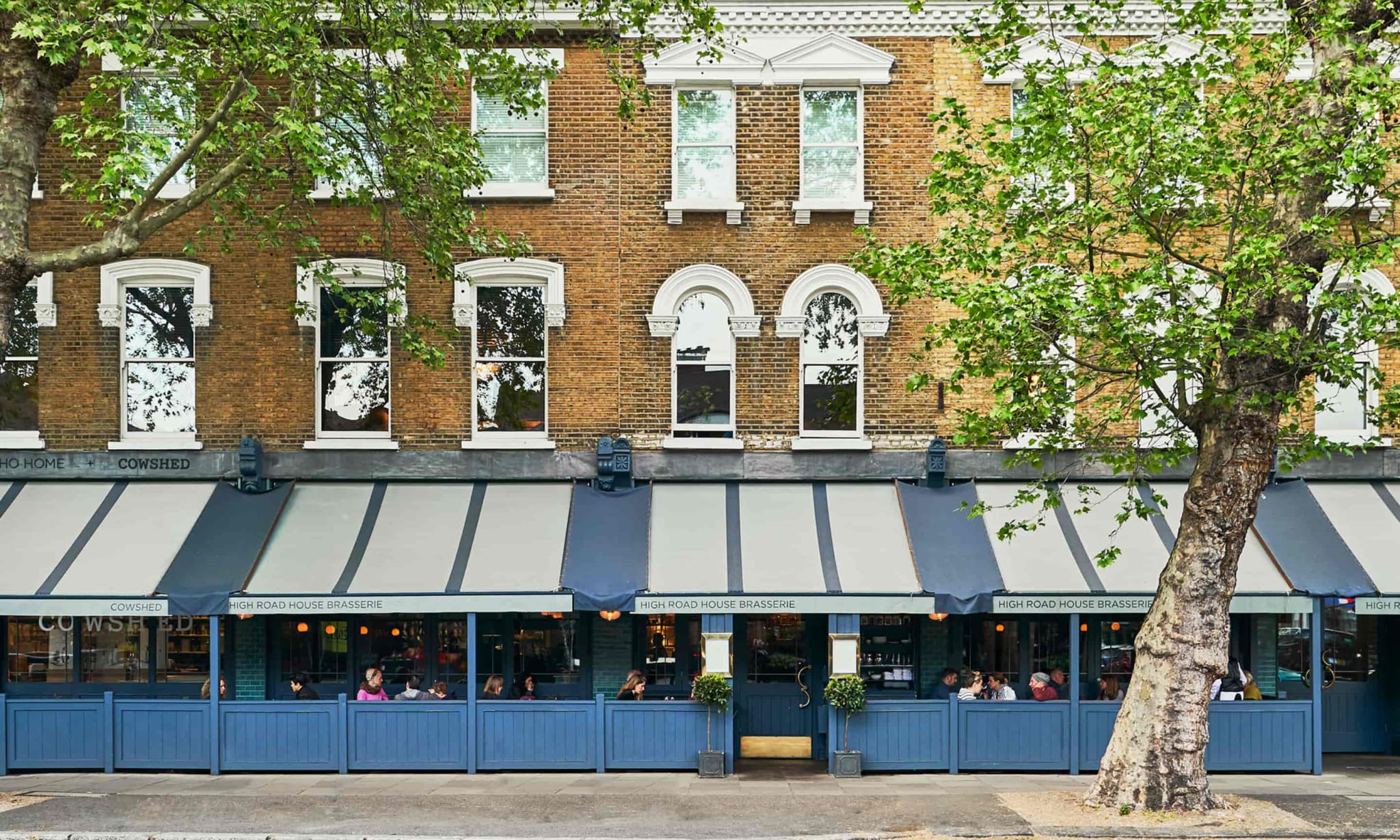 The exterior of a building on a restaurant with a blue restaurant awning over an eating area attached to the front.