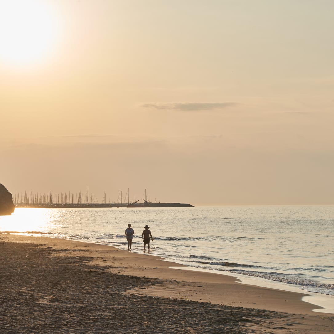 Two people walking down a beach at sunset.