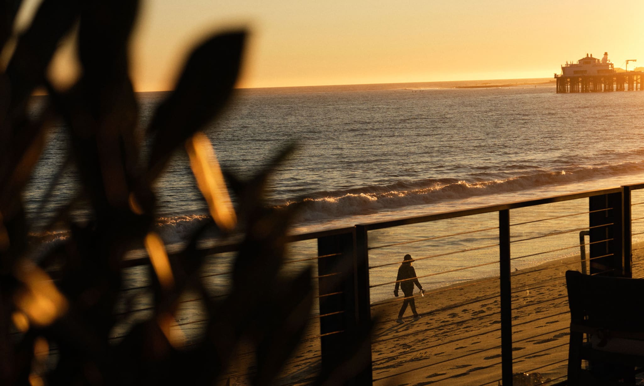 A person walks on a beach at sunset.