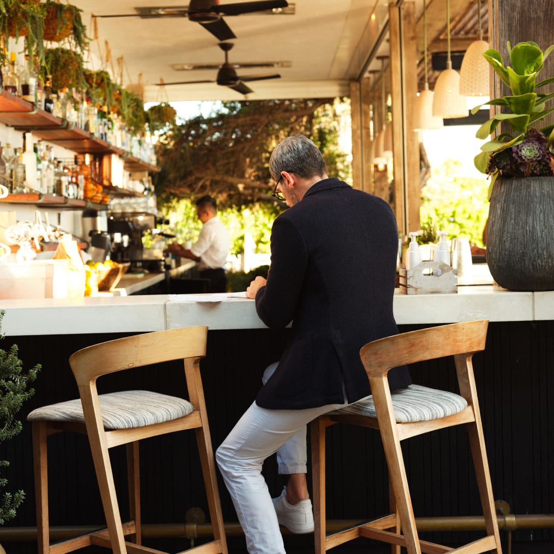 A man sits on a high stool at an outdoor bar.