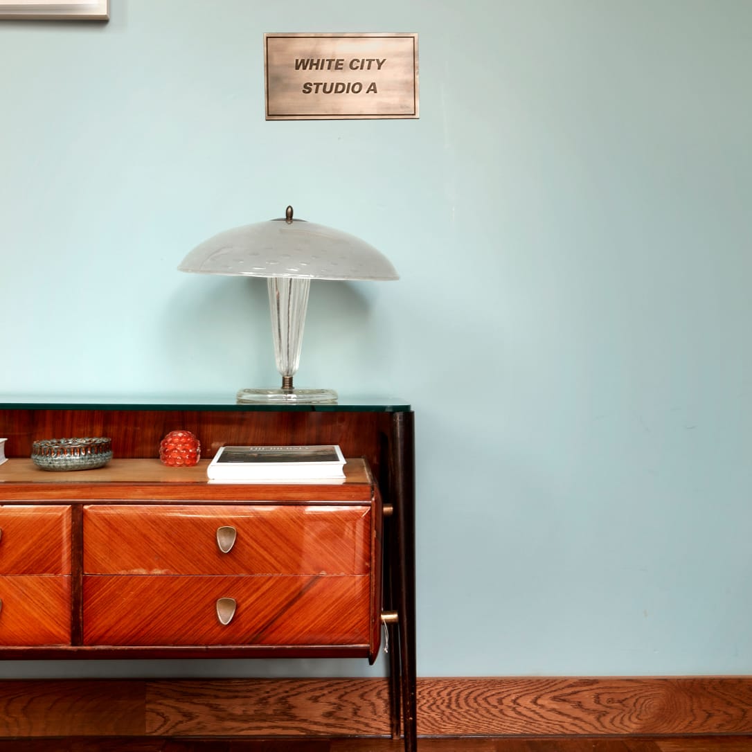 A side table with a lamp on it underneath a sign saying White City Studio A.