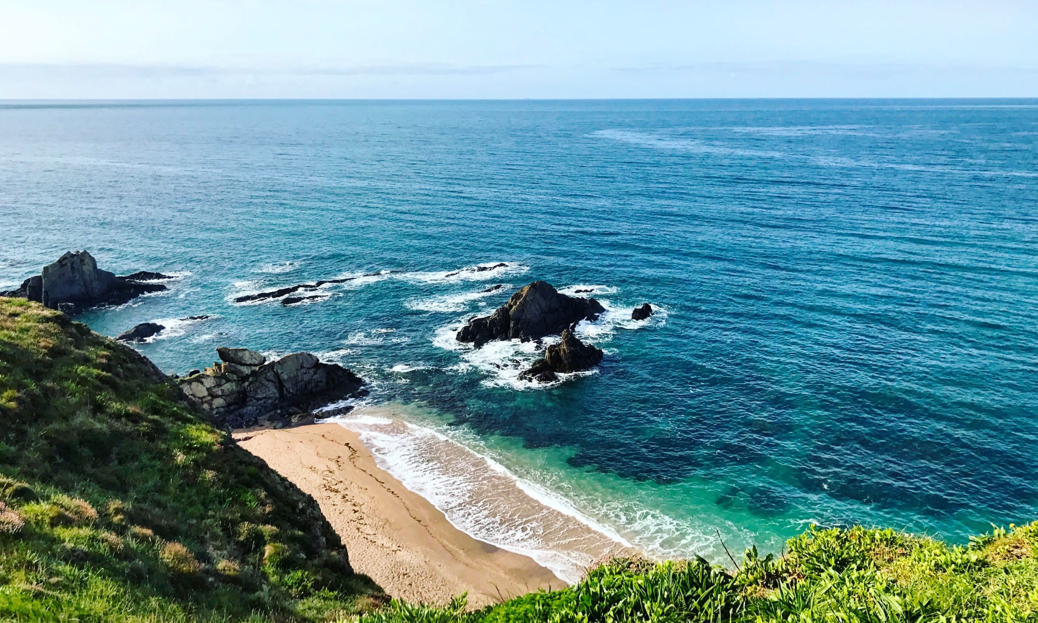 A clifftop looking down at a beach and the sea.