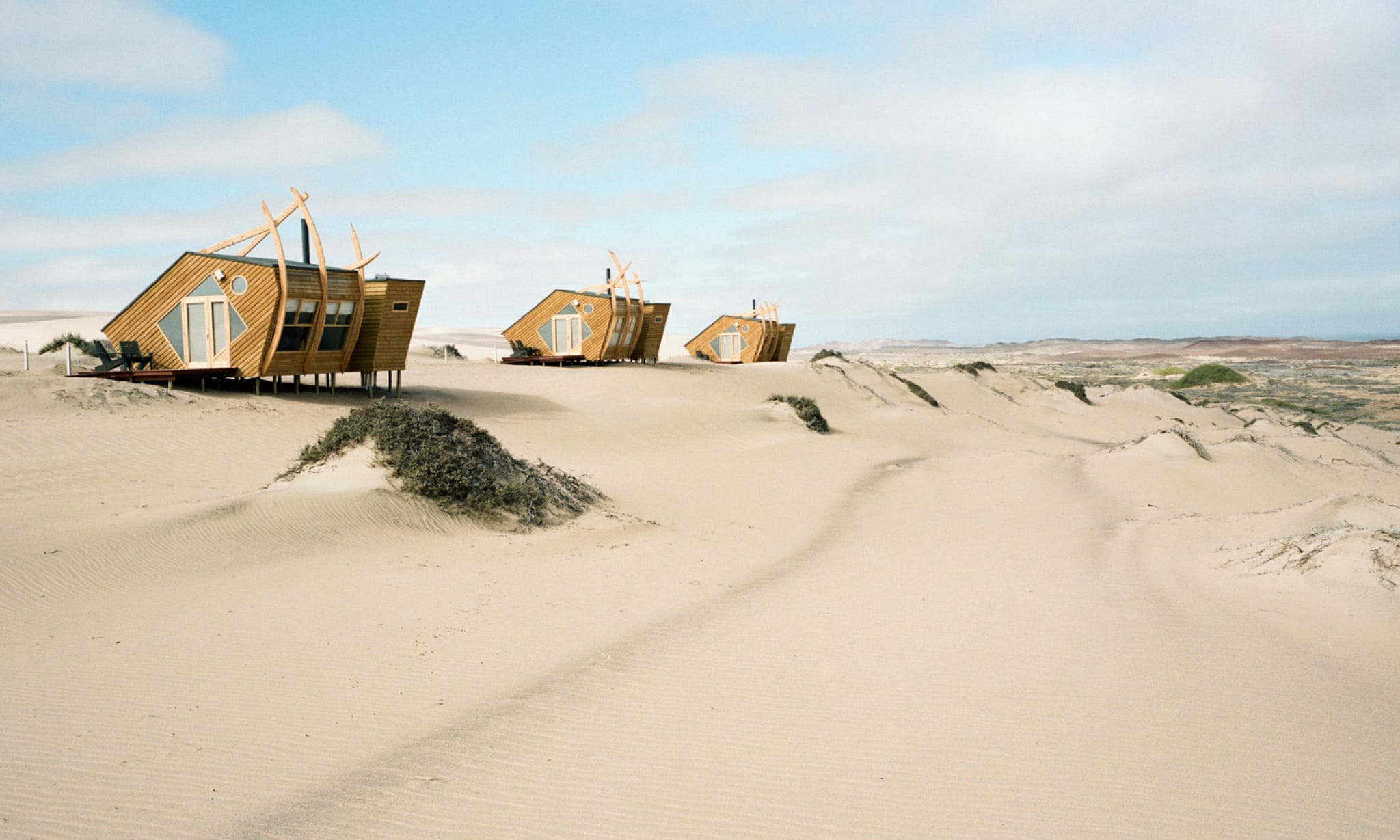 Three wooden buildings perched on a dune in the desert.