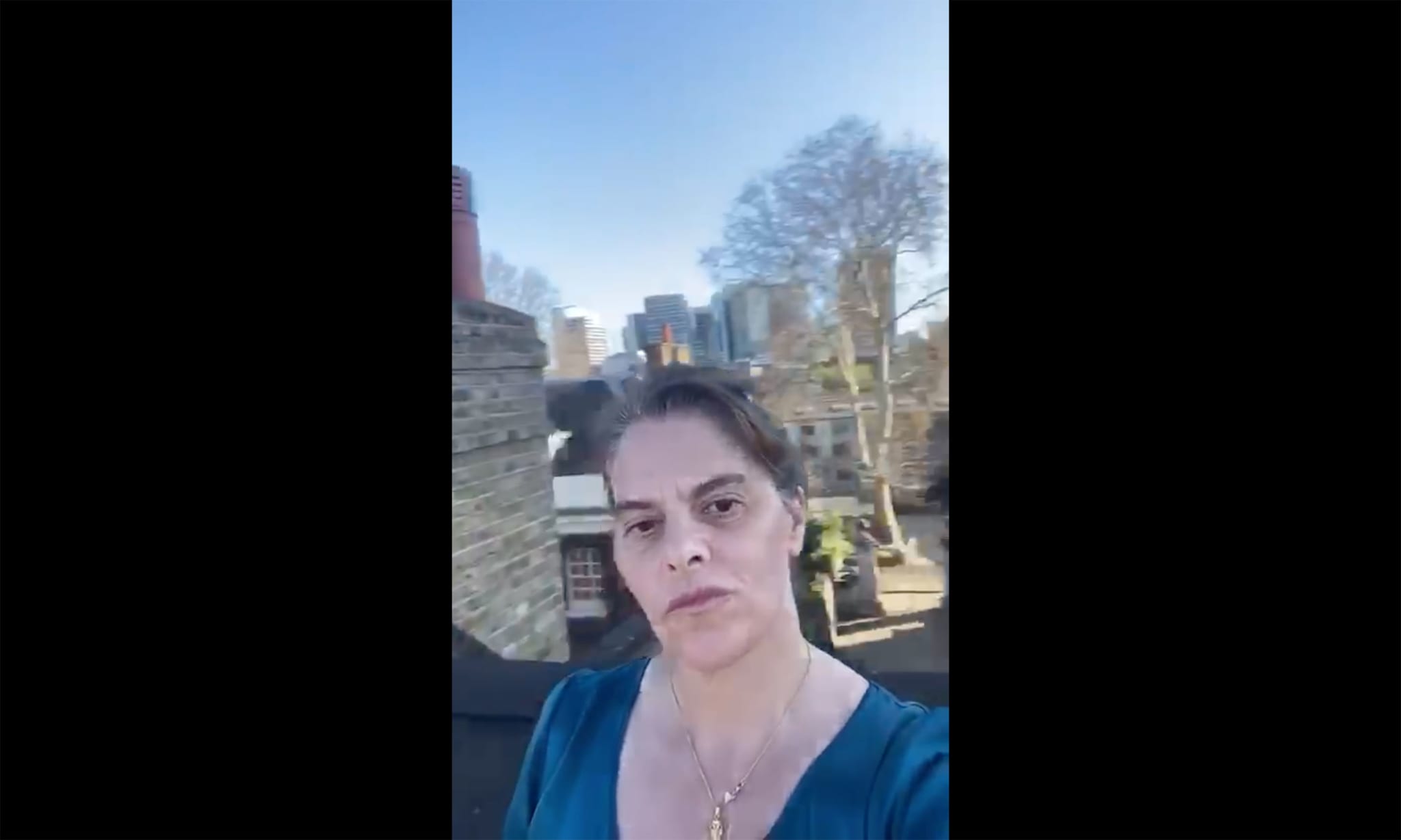 A woman standing on a roof with buildings, trees and a blue sky in the background.