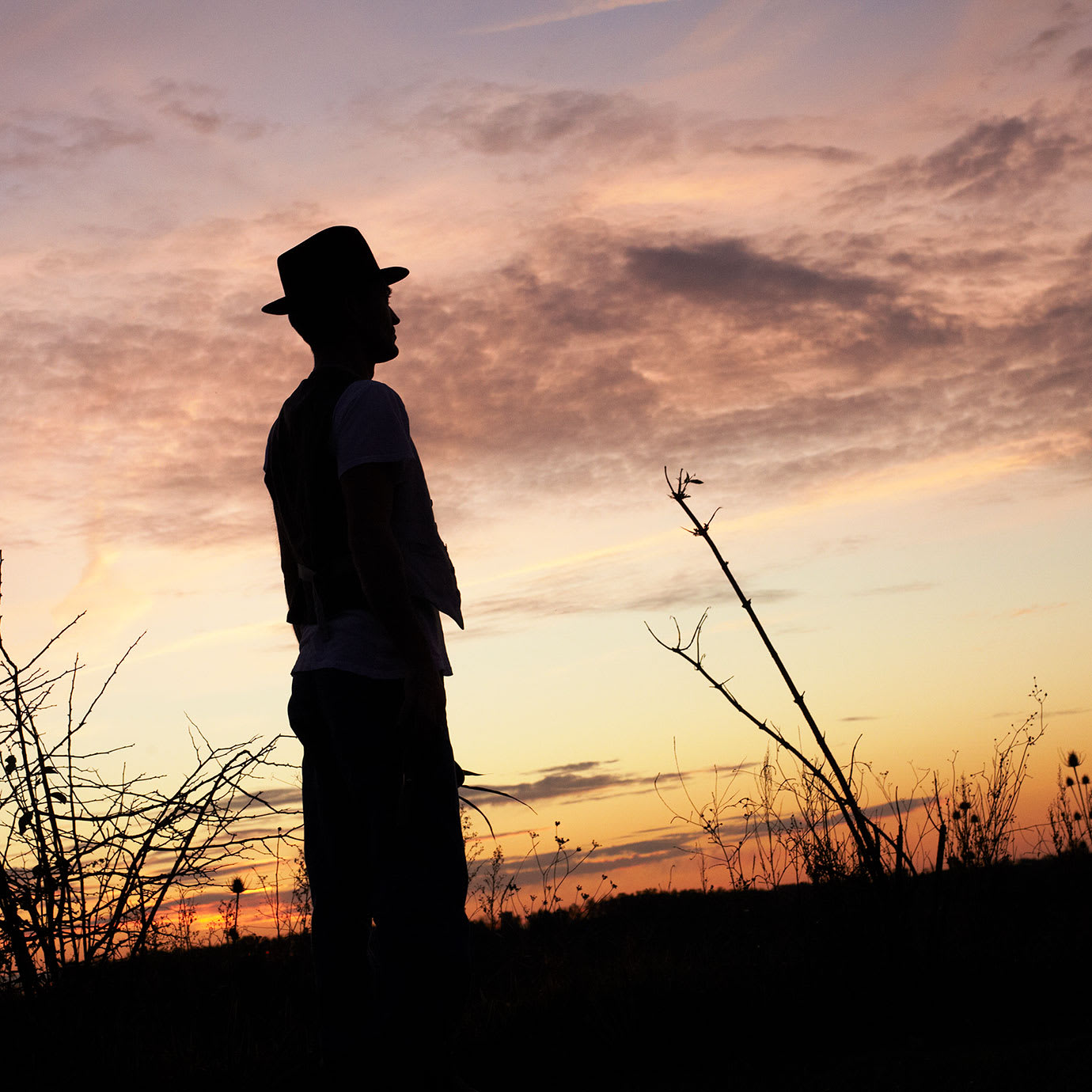 The silhouette of a man standing in a field at sunset.