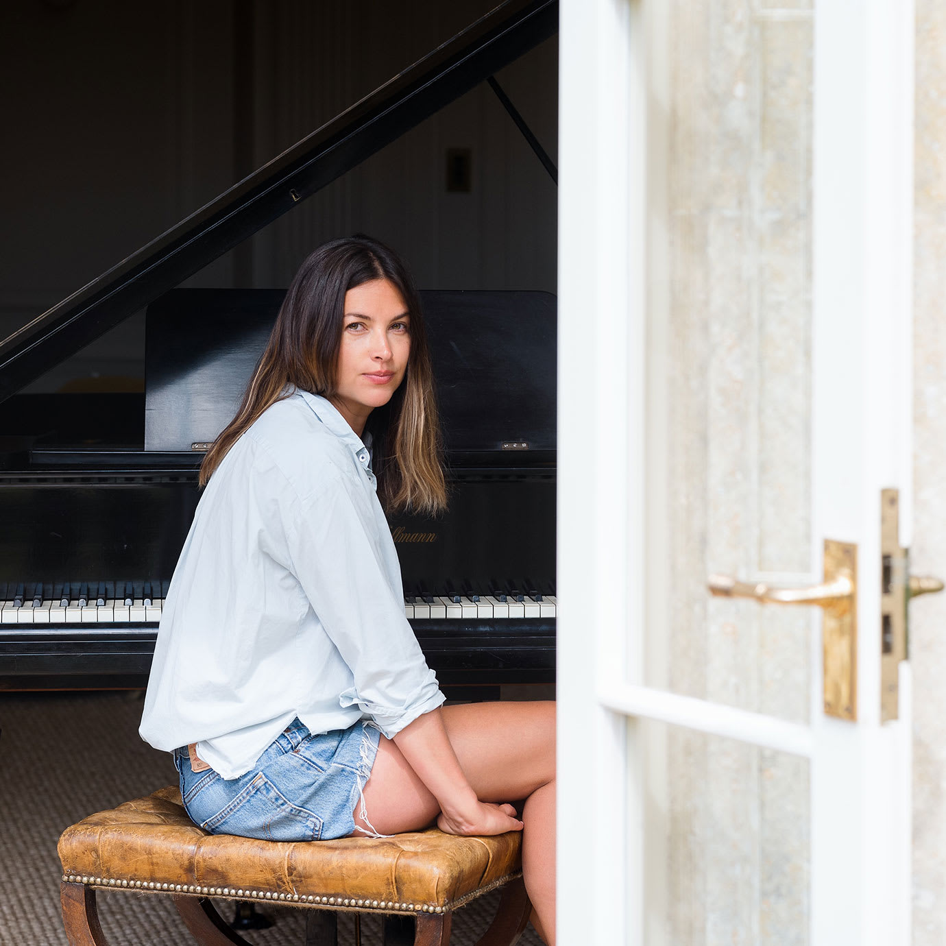 A woman sitting at a grand piano next to an open door.
