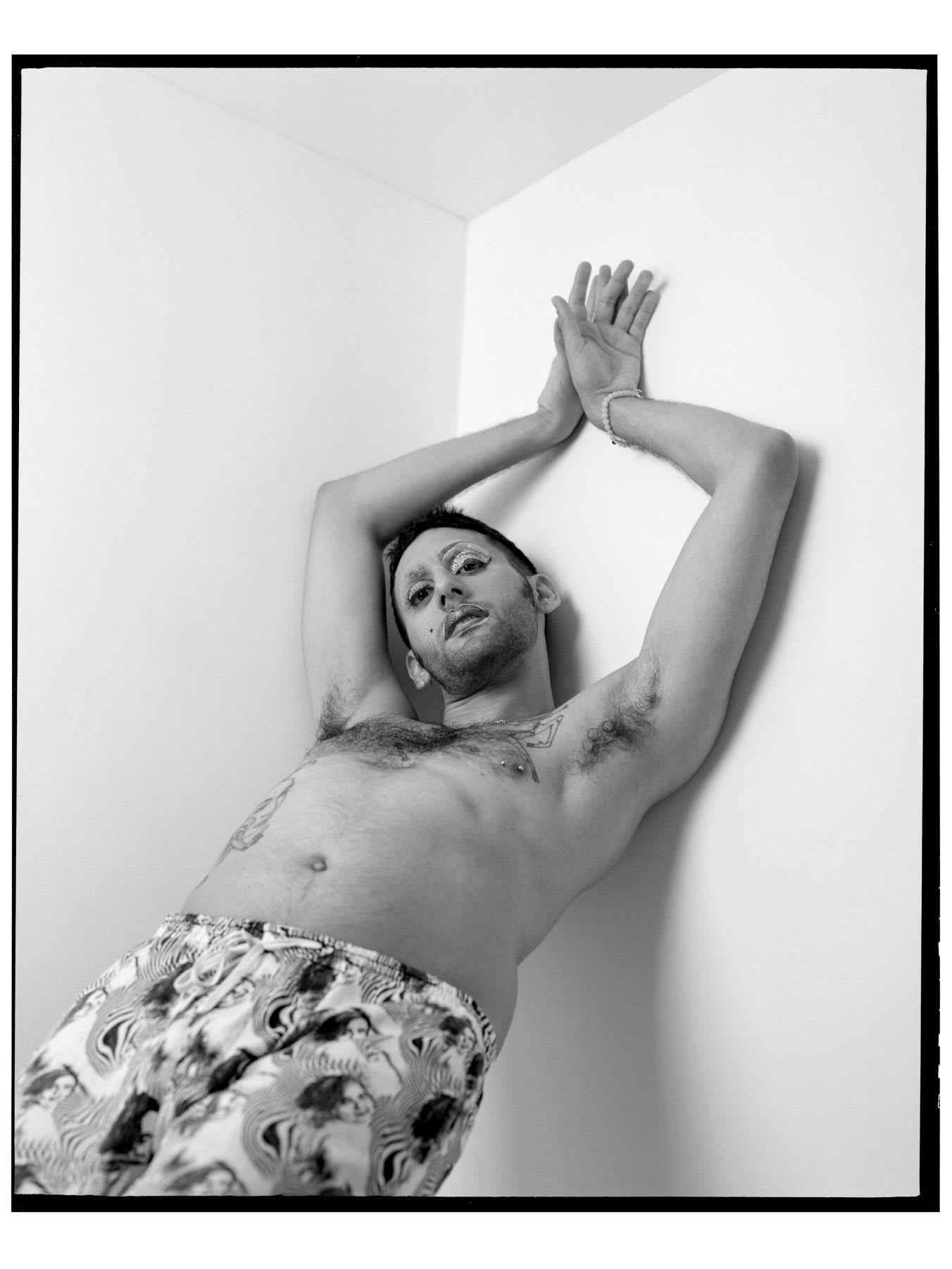 A man with his arms clasped above his head leaning against a plain wall.