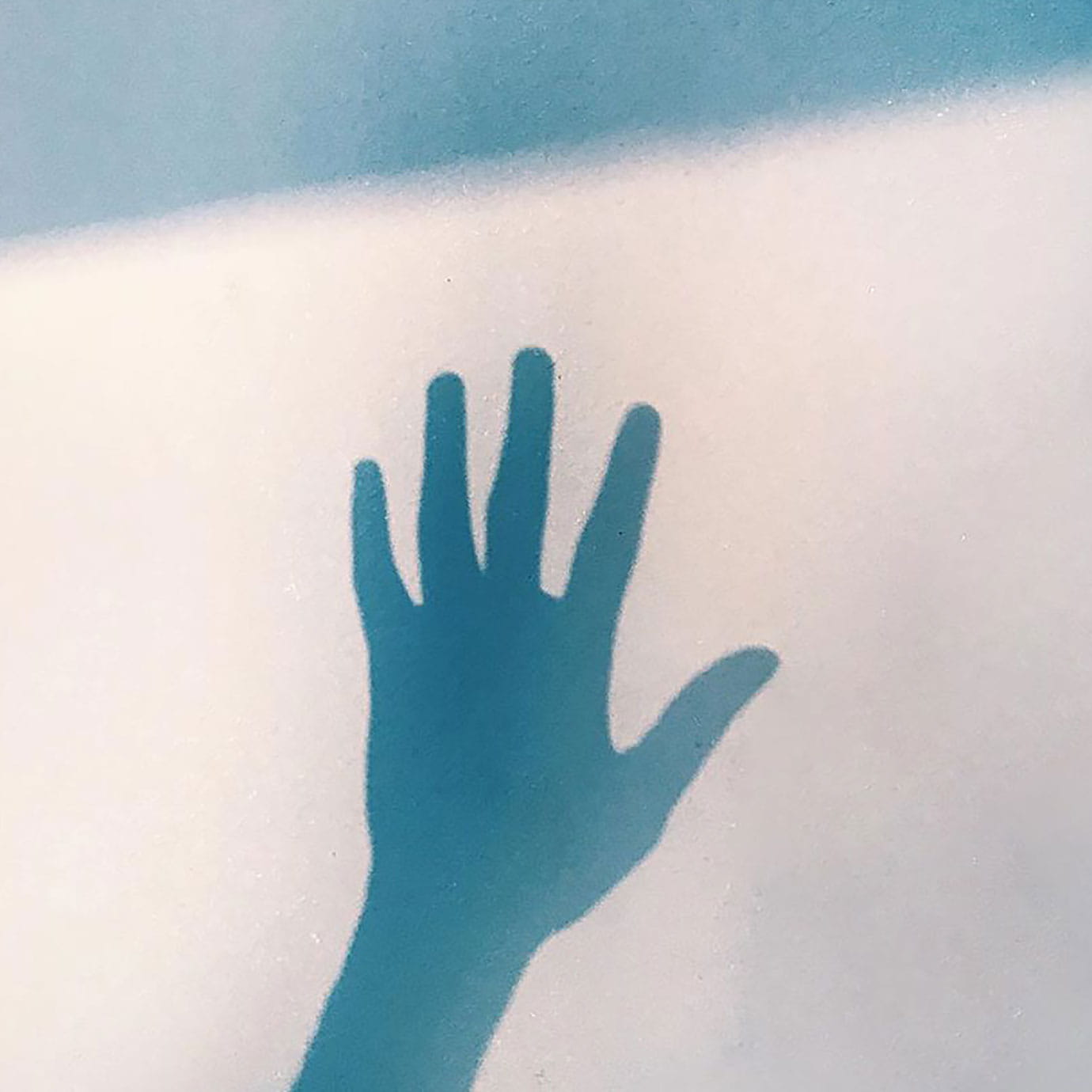 A grainy shadow of a hand on a wall of blue light.