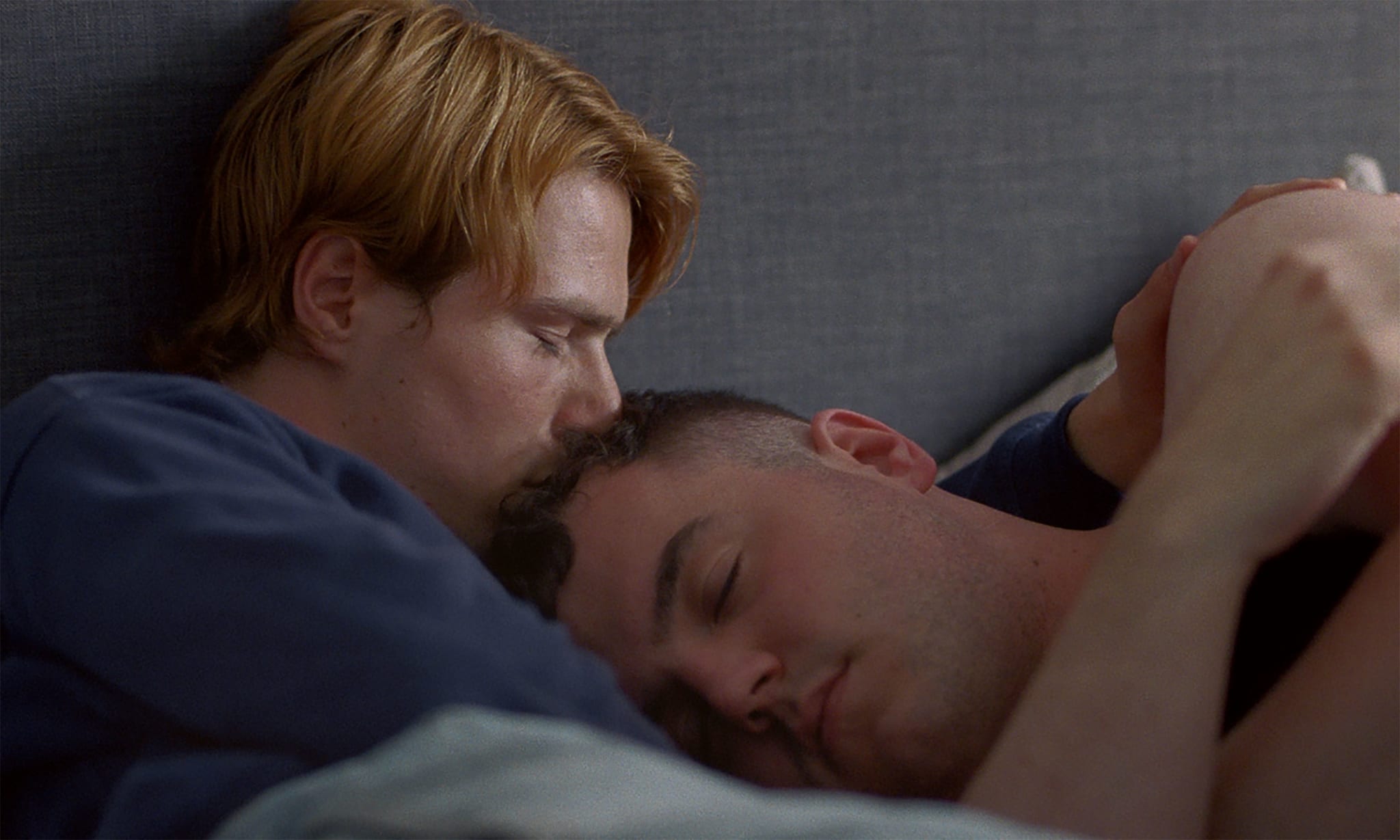 One man comforting another man in bed.