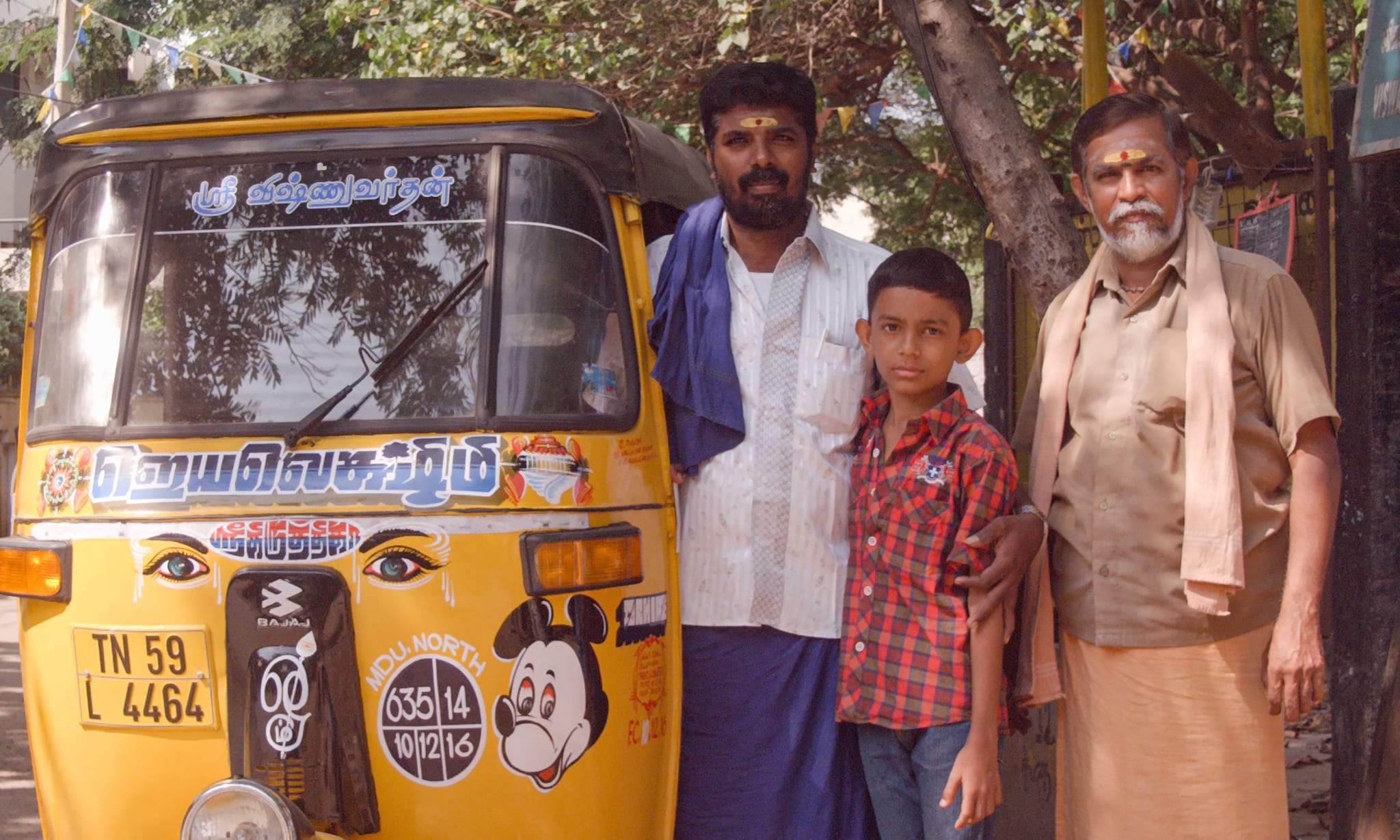Two men and a boy standing next to a yellow tut-tut with a sticker of Mickey Mouse on it.