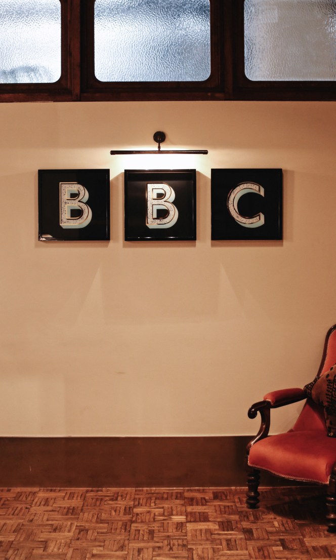 A BBC sign on a wall by a chair.