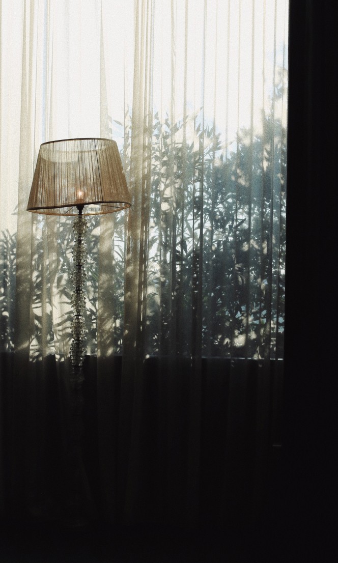 Light spills through a curtain and highlights a lamp.