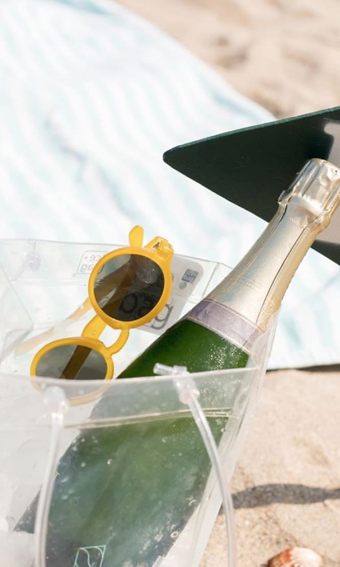 Sunglasses and champagne in a cooler on a beach.