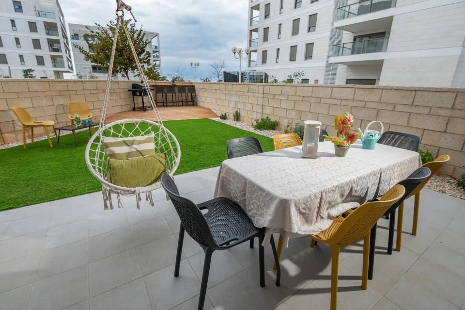החצר של סוויטת נירוונה: שולחן אוכל, כיסא נדנדה תלוי ודשא סינטטי