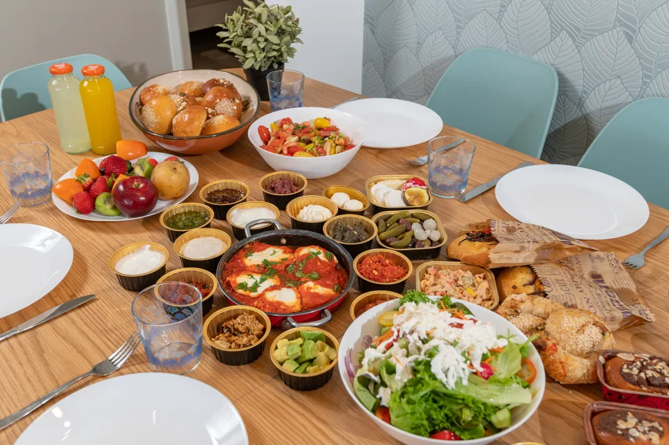 ארוחת בוקר עם שקשוקה, סלטים ולחמניות על שולחן האוכל בסוויטת סנסט