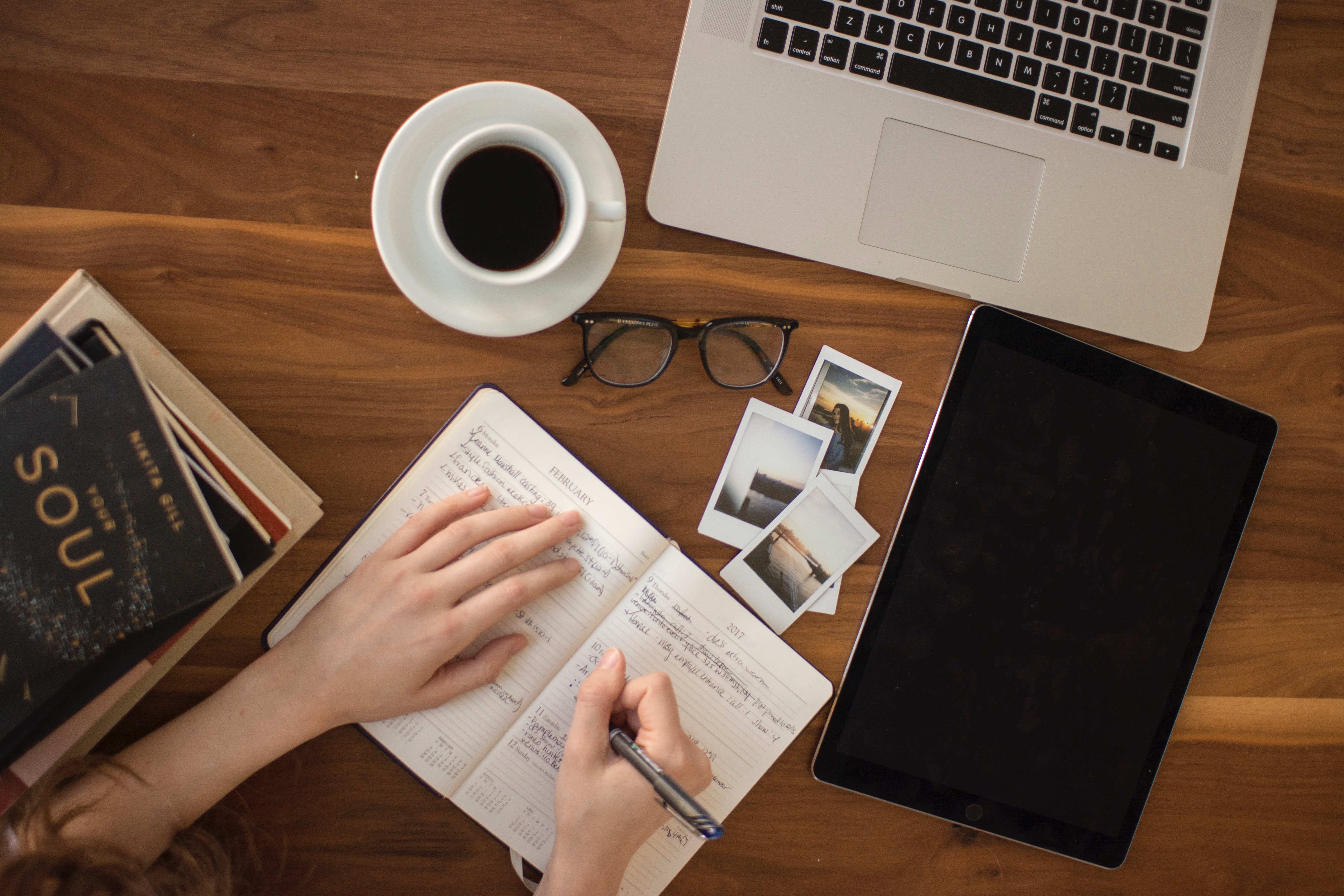 Person writing in a notebook at wooden desk.