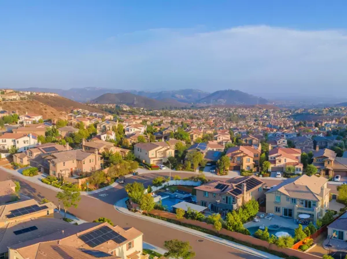 Aerial view of California suburban homes with rolling hills under a clear blue sky.