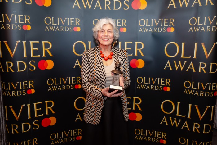 Sylvia Addison holds her Olivier Award statuette in front of a branded backdrop