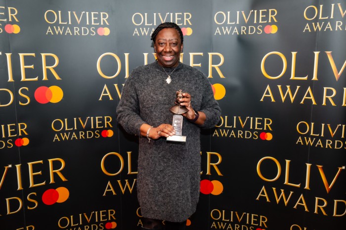 Vereen Irving holds her Olivier Award statuette in front of a branded backdrop