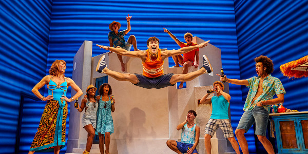 Arcangelo Ciulla as Pepper and Company in MAMMA MIA! Arcangelo is doing splits in the air. Everyone around is cheering him on.