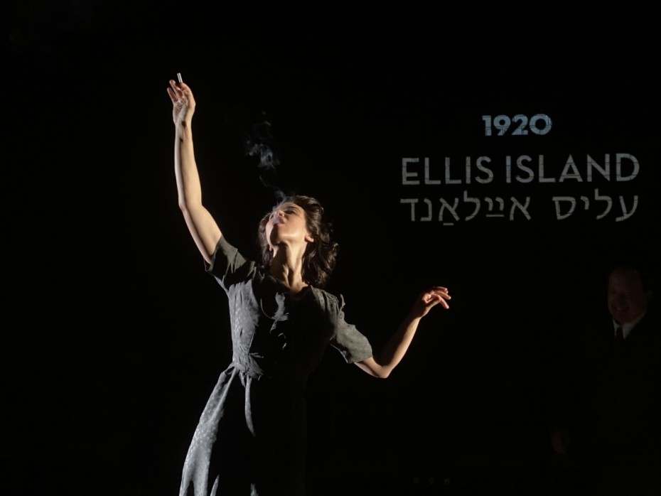 Woman stands with arm lifted to the air wearing a black dress