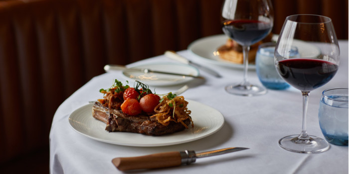 A steak is presented on a plate with tomatoes and a glass of red wine