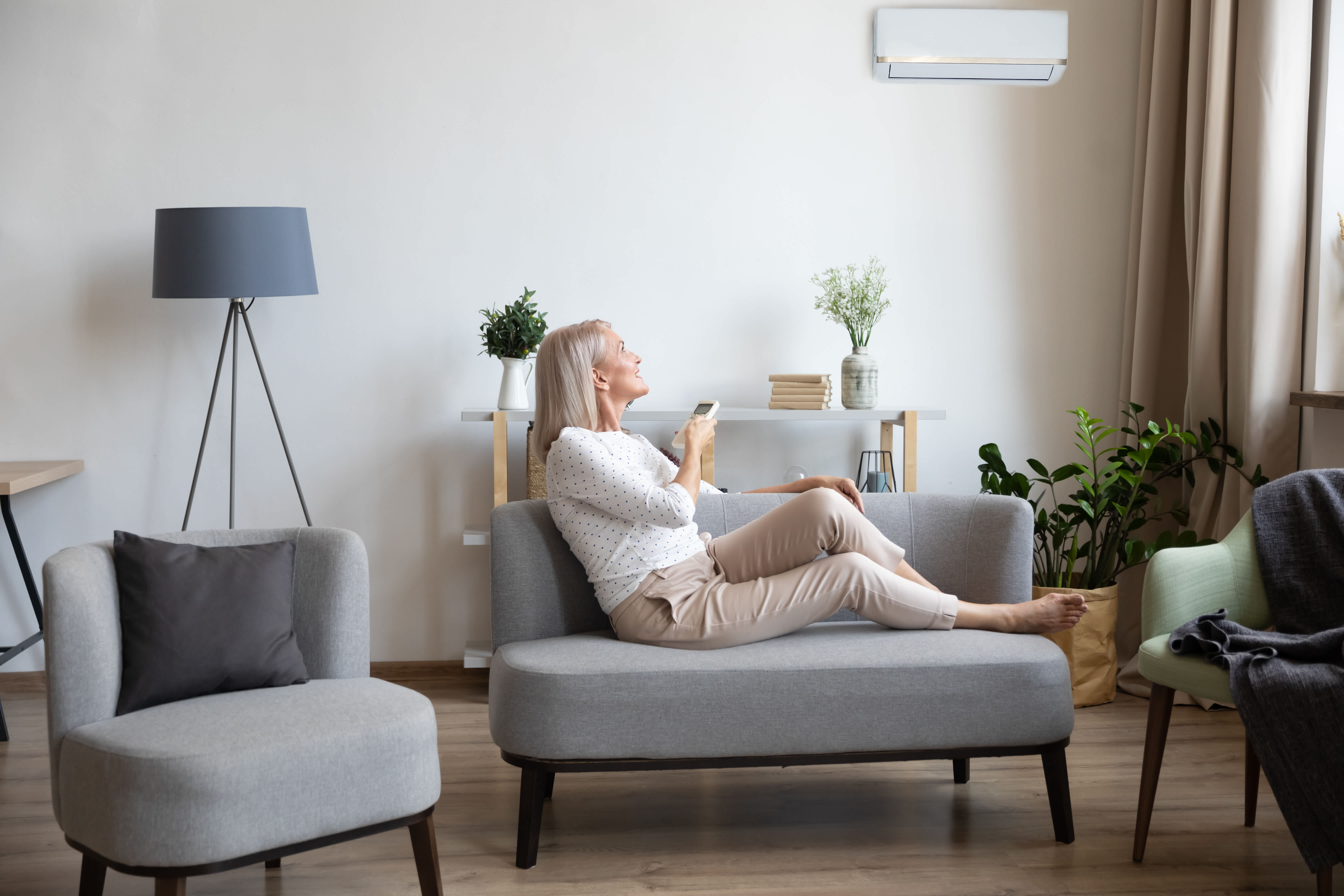 vrouw in living past airco binnenunit aan met afstandsbediening
