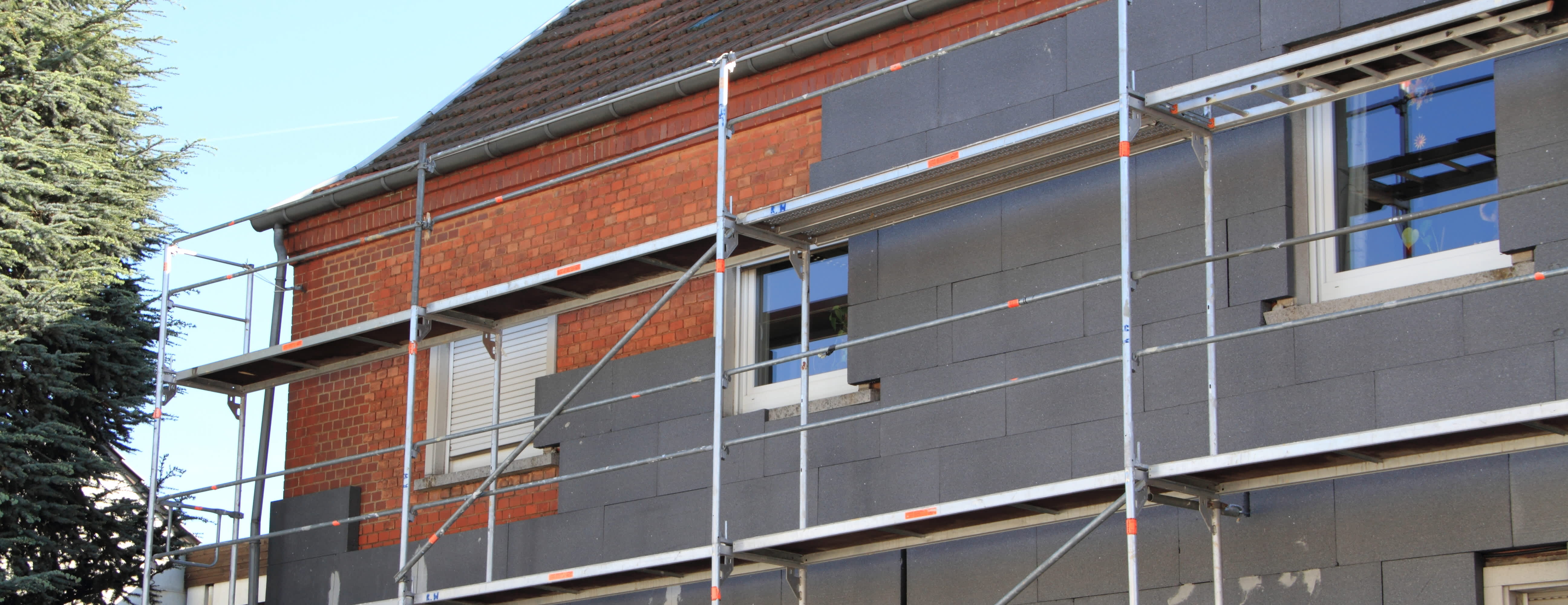 Façade de maison en cours de rénovation avec panneaux isolants gris fixés