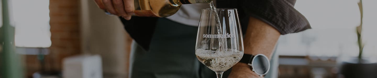 A man pouring white wine into a sommsation branded wine glass