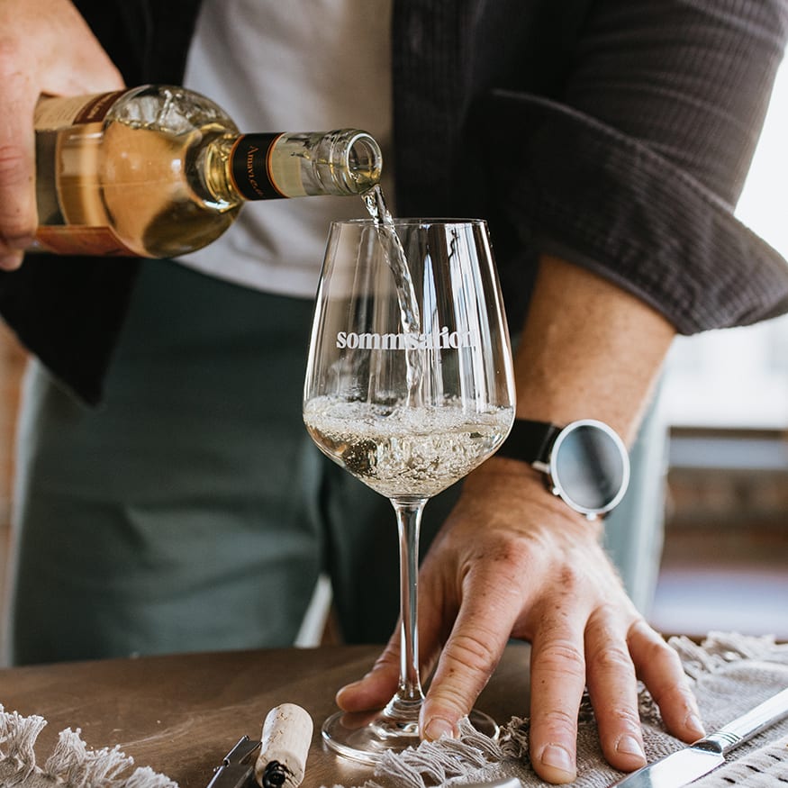 Man pouring white wine into a sommsation wine glass