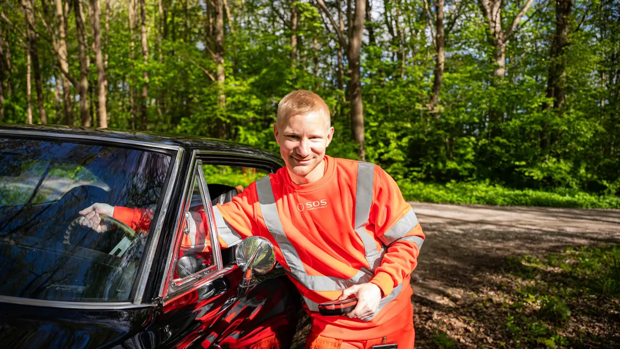 Autoredder med hånd gennem vindue på rat