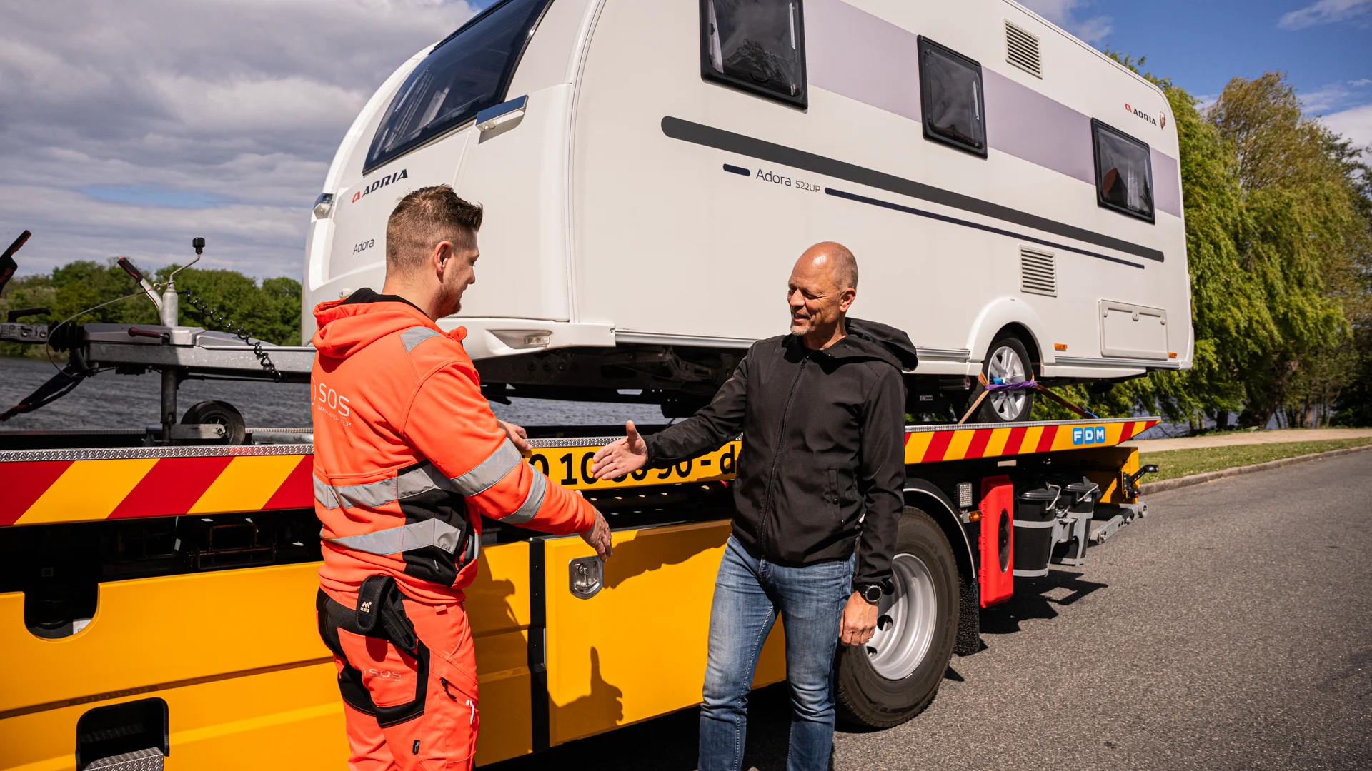 Autoredder og ejer af campingvogn giver hånd. Campingvogn på lad. 