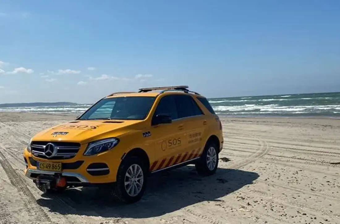 Autoredder bil ses på strand. Billedet taget forfra. I baggrunden ses havet.