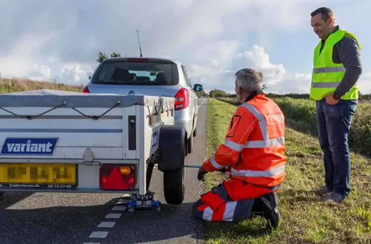 Autoredder sidder på knæ ved lille trailer