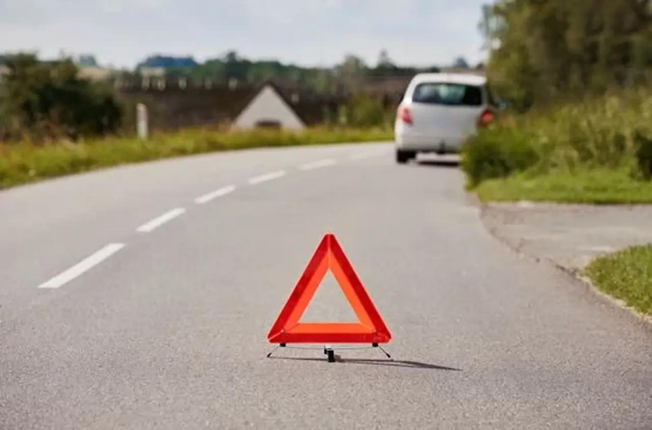Advarselstrekant på landevej. Længere fremme holder hvid bil i vejkanten. 