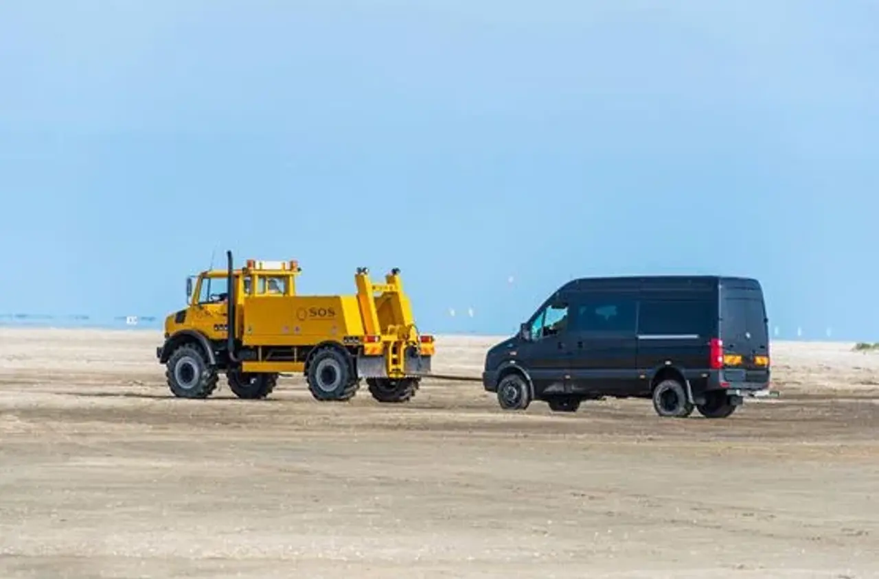 Stor sort bil bugseres på strand af stor autoredderbil