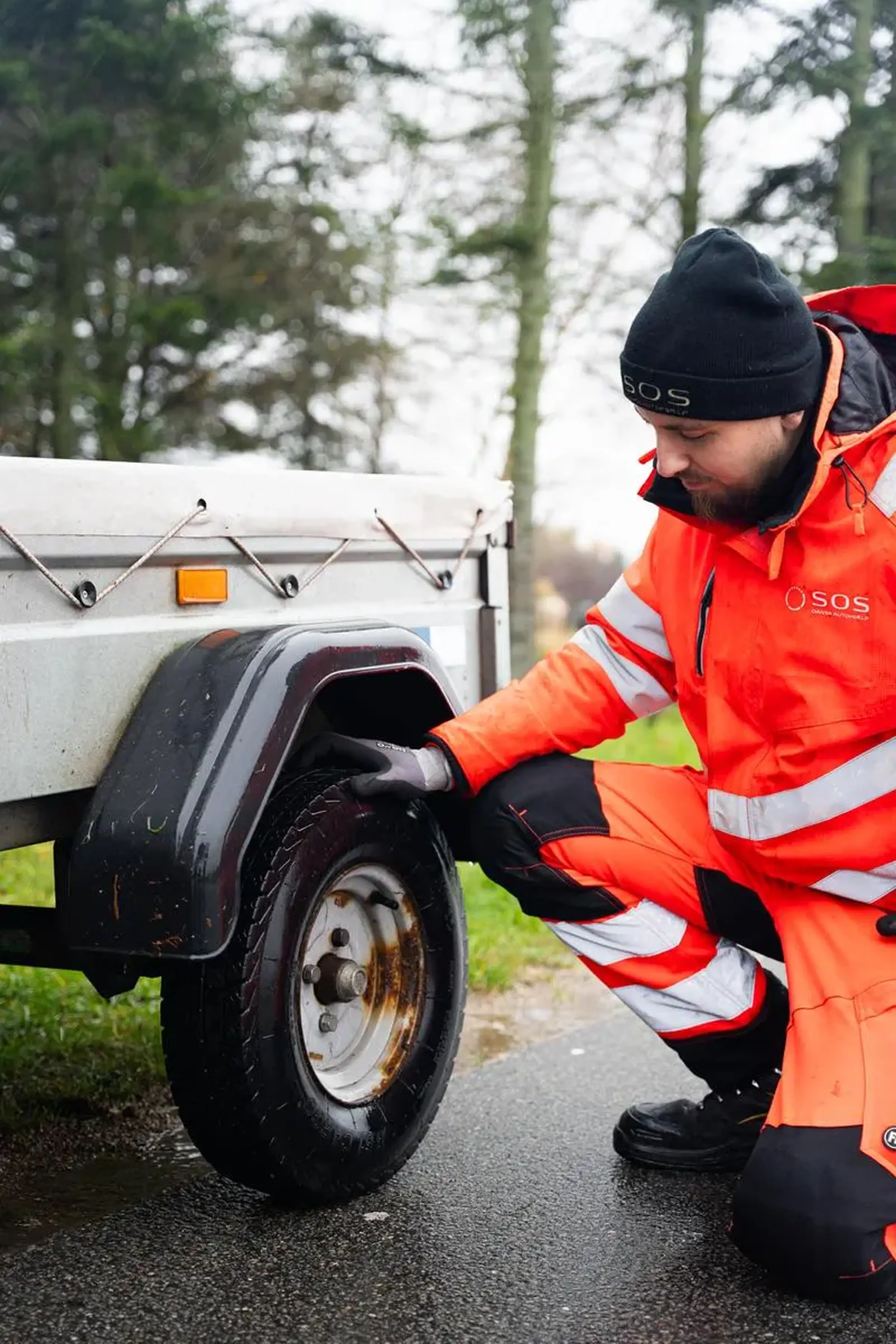 Autoredder sidder på huk ved trailer
