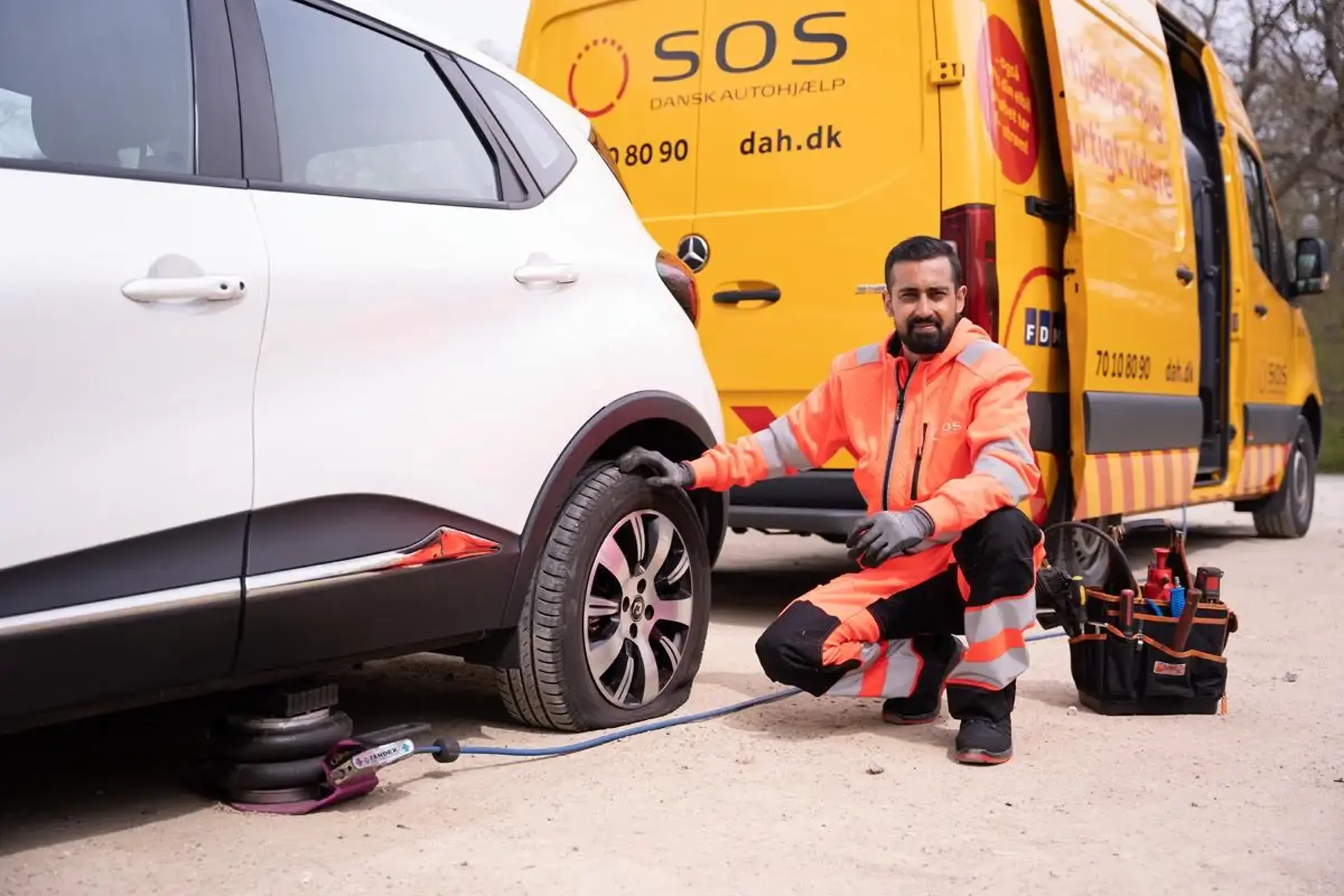Autoredder sidder ved bil og smiler. Bilen er punkteret.